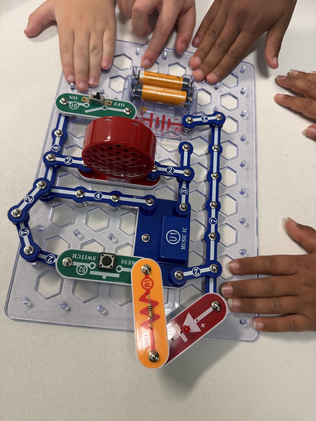 Students' hands building a Snap Circuits musical doorbell